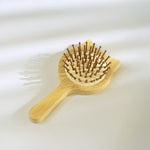 A light natural wood hairbrush with brown bristles, photographed on a clean white background with soft shadows.