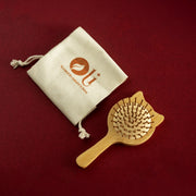 A wooden hairbrush with a handle and cat-shaped ears, shown next to a beige drawstring pouch with a logo, on a dark red background.
