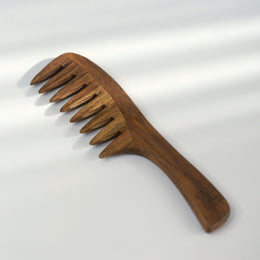 A wooden hair comb with wide, spaced teeth and a curved handle, shown on a clean white background with soft diagonal shadows.