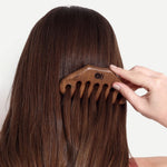 Person using a wooden comb on their hair against a white background