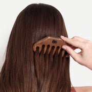 Person using a wooden comb on their hair against a white background