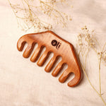 Wooden comb with 'oli' branding on a beige background with dried flowers.