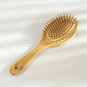 A natural bamboo hairbrush with light tan wood handle and bristles, photographed on a white background with soft leaf shadows.
