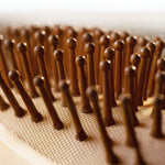 Close-up of a wooden hairbrush with rounded wooden bristles standing upright on a beige mesh surface.
